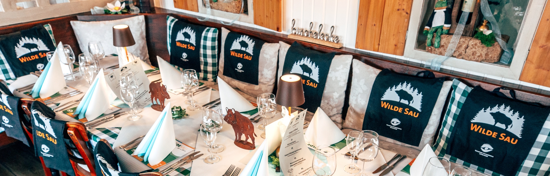 Tischdekoration zur 'Wilde Sau'-Veranstaltung mit Servietten, Lampen, Wildschwein-Deko und Logo-Taschen im rustikalen Raum.