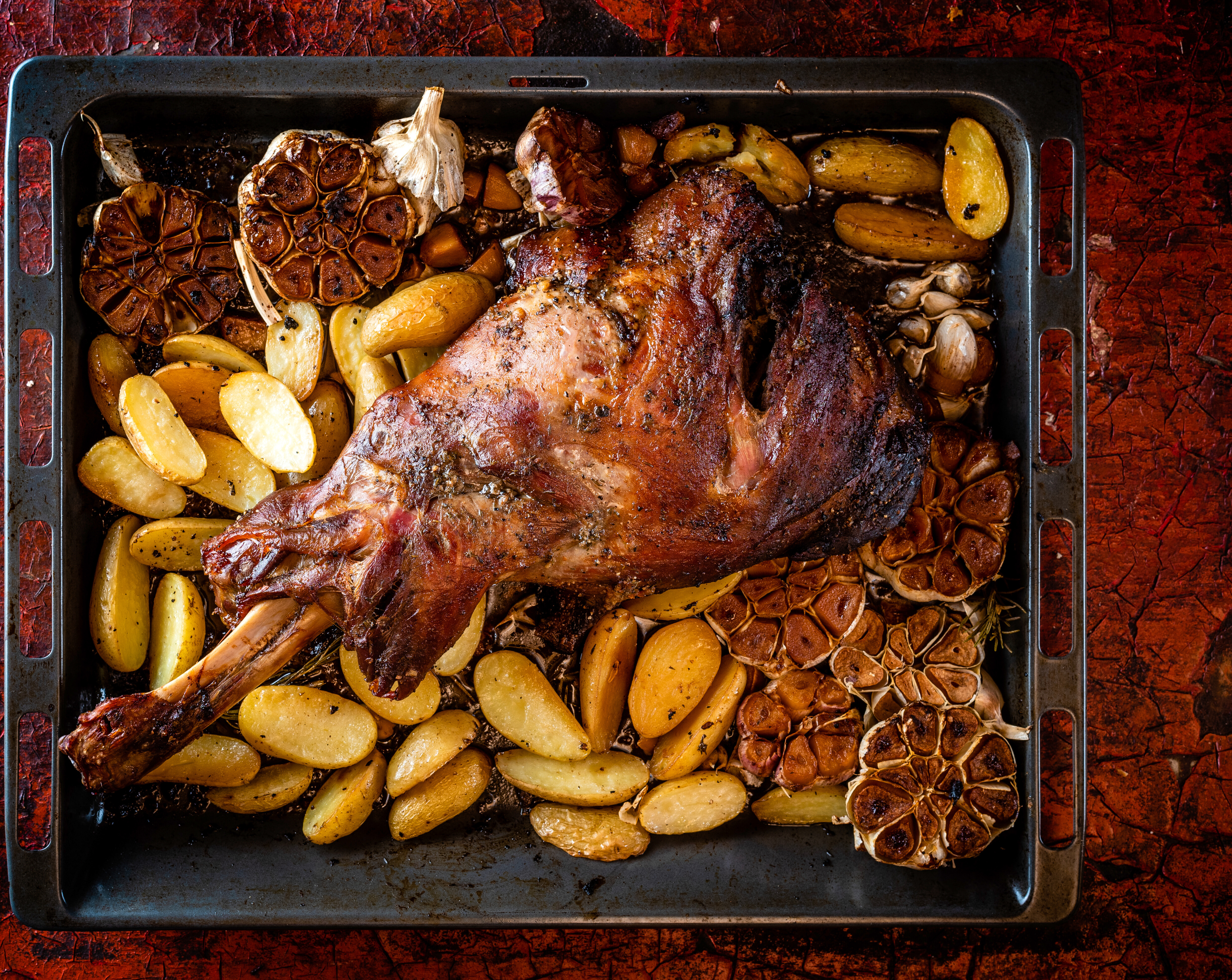 Wildschweinschulter mit gerösteten Kartoffeln und Knoblauch auf Ofenblech.